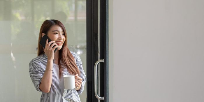 Smiling asian woman talking on the phone at home, happy young girl holds cellphone making answering call, attractive teenager having pleasant conversation chatting by mobile with friend