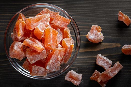 Natural farm homemade candied pumpkin fruits sprinkled with powdered sugar in a glass bowl on a wooden table, topview