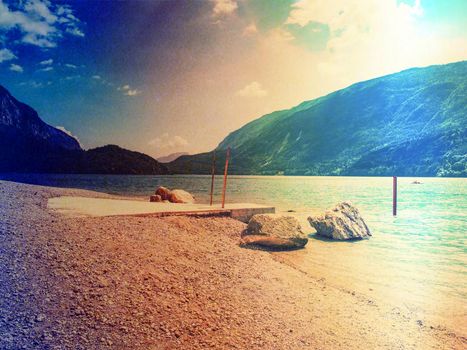 Jet pier and pebbles beach at bblue alpine lake. Warm sunrays over hills.  Abstract.