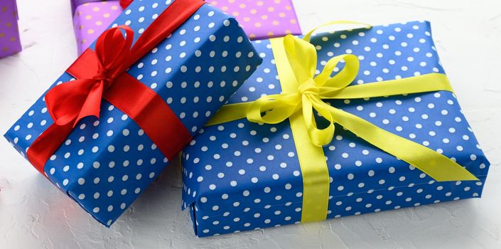 boxes packed in festive blue paper and tied with silk ribbon on white background, birthday gift, surprise, close up