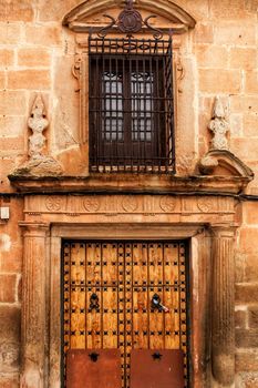 Old stone facade made of carved stone and vintage wooden door in a majestic house in Villanueva de los Infantes, Ciudad Real community, Spain