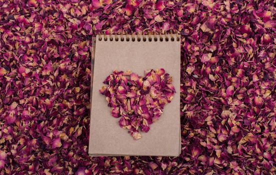 Dry rose petals form a heart shape  on a spiral notebook