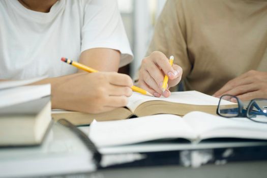 Learning, education and school concept. Young woman and man studying for a test or an exam. Tutor books with friends. Young students campus helps friend catching up and learning.