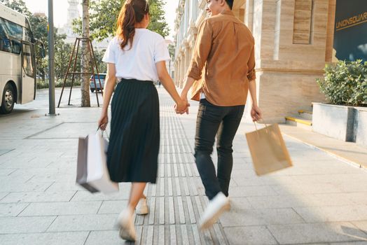 Lower body section of a young tourist couple walking by store windows and holding paper shopping bags in a destination city.