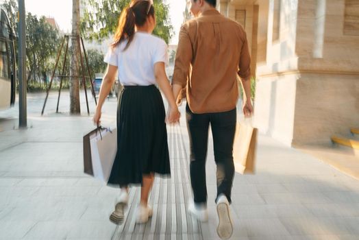 Lower body section of a young tourist couple walking by store windows and holding paper shopping bags in a destination city.