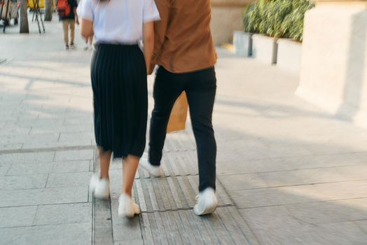 Lower body section of a young tourist couple walking by store windows and holding paper shopping bags in a destination city.