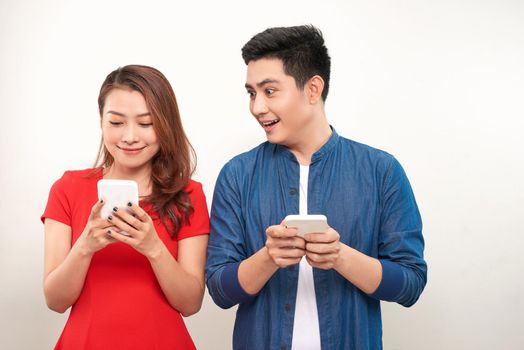 Asian couple using gadgets: pretty girl typing a message on cell phone while her boyfriend standing next to her, looking down at the screen of her smart phone