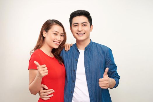 Young couple over isolated background smiling with happy face looking and pointing to the side with thumb up