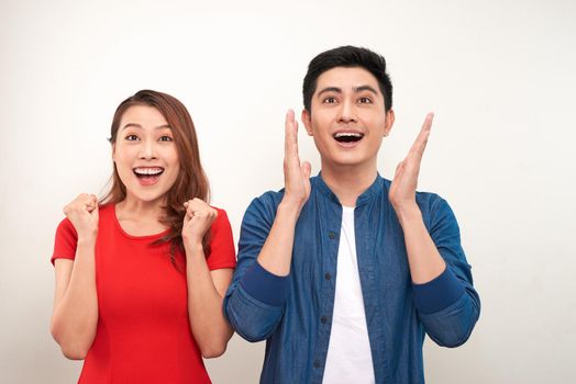 Young asian couple in love over isolated background celebrating surprised and amazed for success with arms raised and open eyes