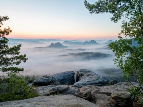 Beautiful morning view Saxony Switzerland. Sandstone peaks and hills increased from foggy background, the misty horizon  is orange due to the first sun rays.