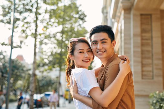 Rear view of a young couple hugging in a destination city while standing in the shopping district near a luxury quality shoe store, outdoors