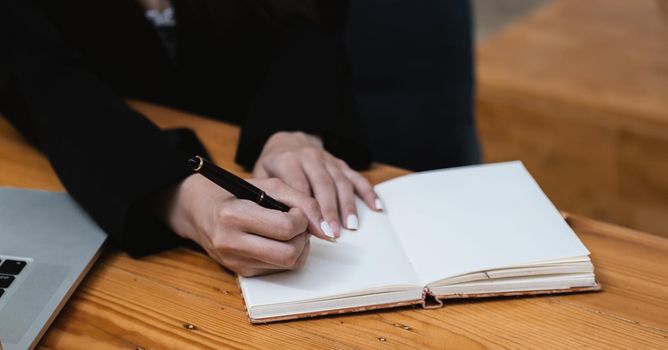 Close up hand of woman hand holding pen taking note and working with laptop at the table office.