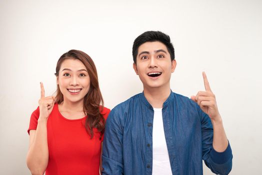 Cheerful asian couple standing isolated over white background, pointing fingers 