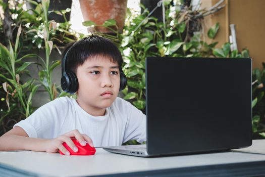 Asian boys wear wireless headphones and use laptop computers to study online and search the Internet.
