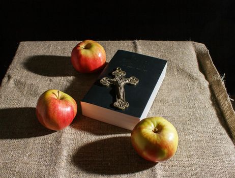 bronze cross, holy bible and three red apples on the table. closeup on black background