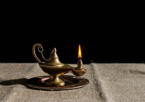 burning magic lamp of aladdin on table. indoor closeup on black background