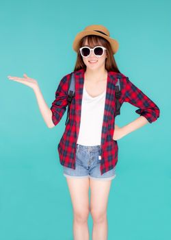 Beautiful portrait young asian woman wear sunglasses and hat smile and enjoy in summer gesture presenting something isolated on blue background, tourist girl in vacation travel concept.