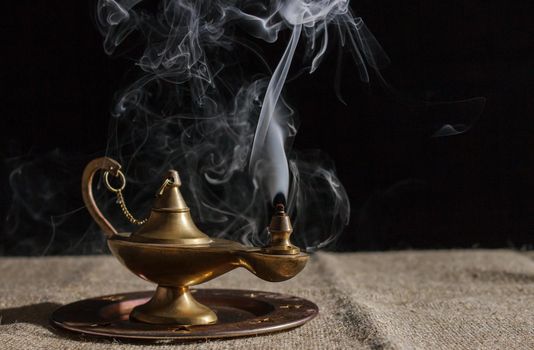 aladdin's magic lamp smokes on table. indoor closeup on black background