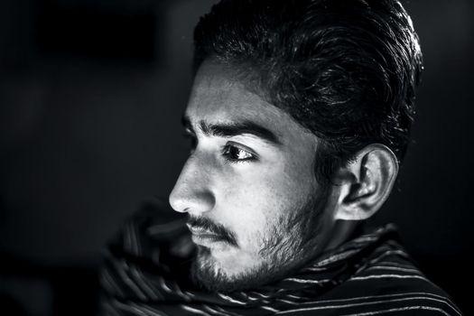 Portrait shot of man in black and white color isolated on black expressing angriness on his face and wearing black colored cloth on his face.