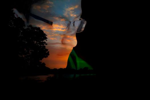Double exposed portrait shot of a teenager wearing green colored hooded t-shirt and looking backwards.Shot manipulated with sunset time shot of a lake.