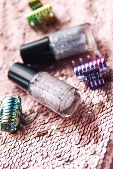 Bright composition of fashion accessories. Nail polishes and hair pins on glitter sequins surface.