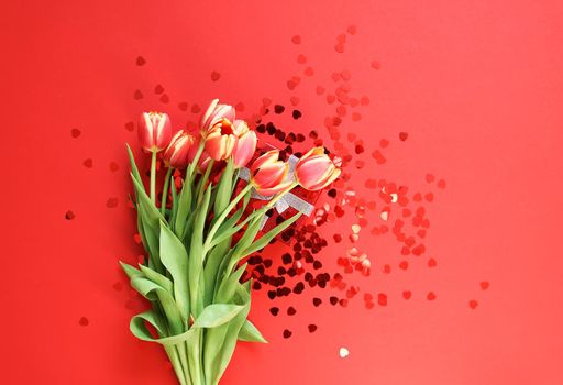 Spring beautiful tulip flowers on red bright background with small heart tinsel. Mother's day, greeting card festive decorative floral composition.
