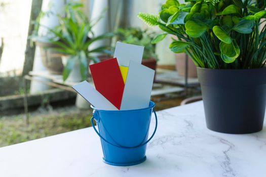 Colorful paper inside of a blue bucket on a white table with garden background