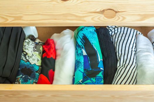 Open light wooden dresser drawer with colorful clothes.