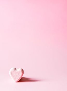 Pink small bath bomb in the shape of heart on soft pastel background