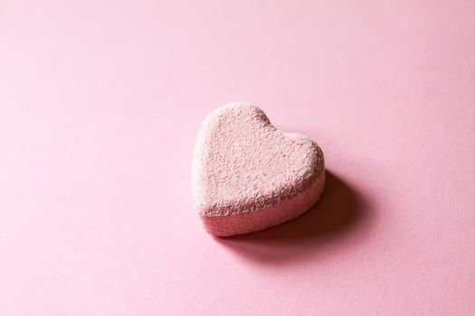 Pink small bath bomb in the shape of heart on soft pastel background