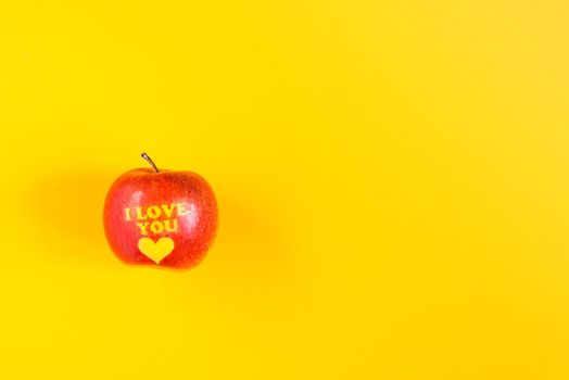 Fresh red apple with words I love you and heart on bright yellow background.