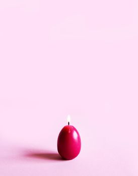 Traditional Easter decor. Group of bright burning paraffin candles in the shape of colorful eggs on soft pink background.