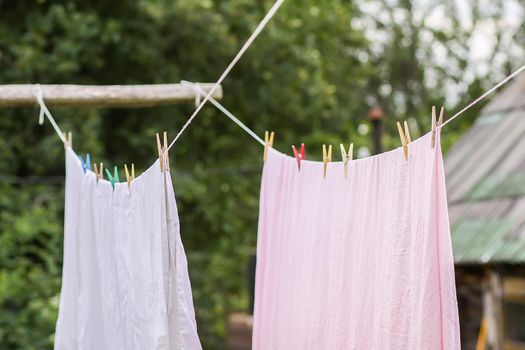 Freshly washed bed linen hanging on the rope outdoors. Clothes drying in rural yard.