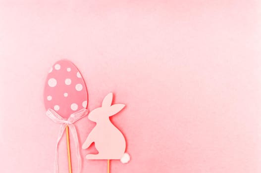 Easter composition with traditional decor. Wooden decorative egg and rabbit figures on soft light pink background