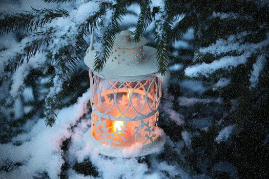 Christmas lantern with burning candle on winter snowfall background.