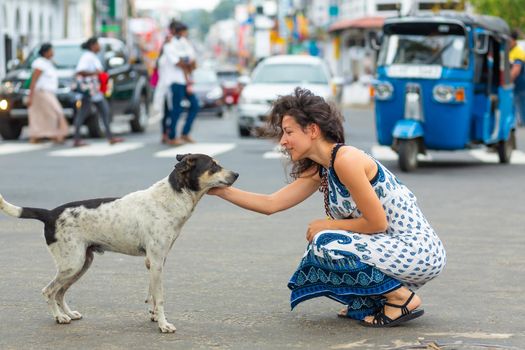 The girl communicates with a stray dog on the street. Pet the dog.