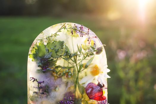 Ice cube with flowers on green grass at summer.