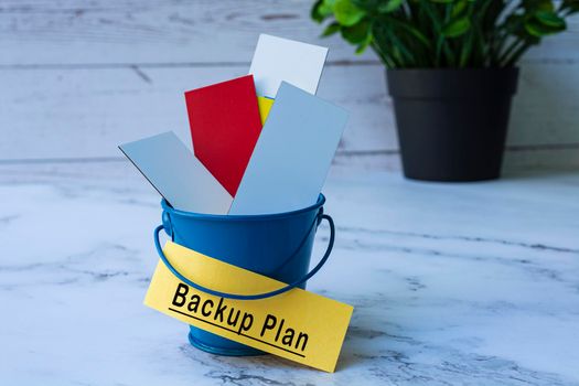 Backup plan text on yellow paper with colorful paper inside of a blue bucket