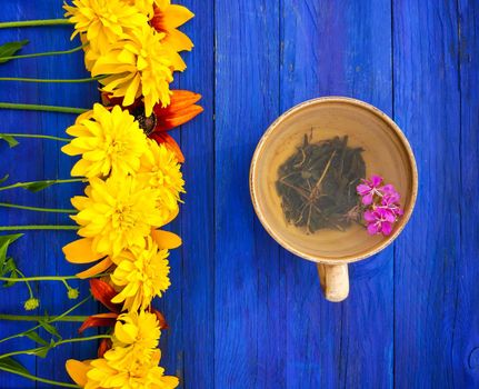 Natural herbal tea with purple fresh flowers and leaves of medical fireweed plant n ceramic cup on blue wooden boards outdoors.