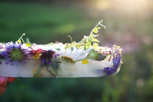 Ice cube with flowers on green grass at summer.