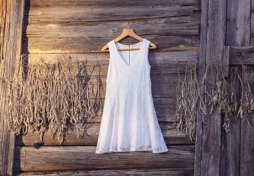 Linen dress hanging on a hanger outdoors on wooden rough wall background