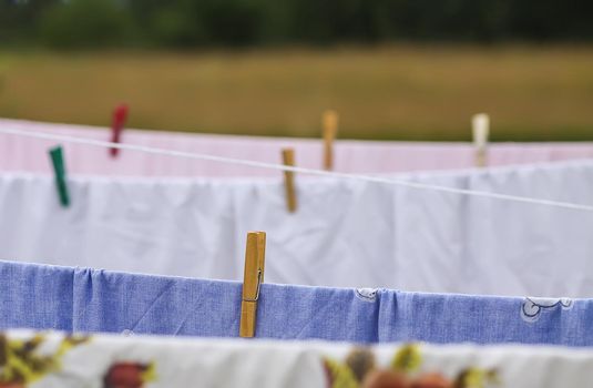 Washed colorful cotton bed sheets hanging on a clothesline outdoors.