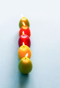 Traditional Easter decor. Bright burning paraffin candles in the shape of colorful eggs on blue background.