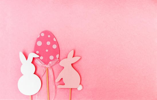 Easter composition with traditional decor. Wooden decorative egg and rabbit figures on soft light pink background