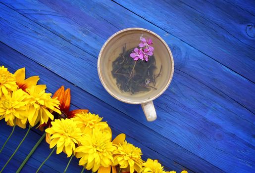 Natural herbal tea with purple fresh flowers and leaves of medical fireweed plant n ceramic cup on blue wooden boards outdoors.