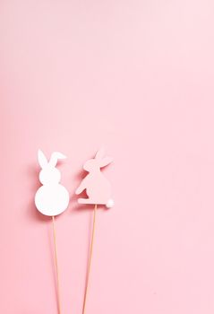 Easter vertical composition with traditional decor. Two rabbit decorative figures on wooden sticks on soft pink background.