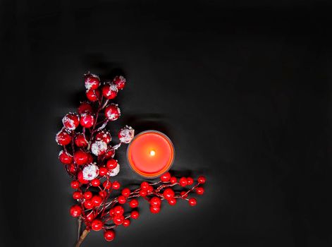 Festive Christmas or New Year composition with red holly berries in snow and burning wax candle.