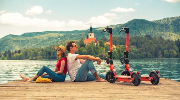 Young couple using electric scooter as modern ecological mean of transport while exploring green country Slovenia at vacations. Green eco energy concept with zero emission. Warm sunshine filter