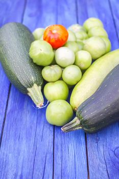 Zucchini and unripe tomatoes. Fresh raw organic vegetables on wooden boards outdoors.