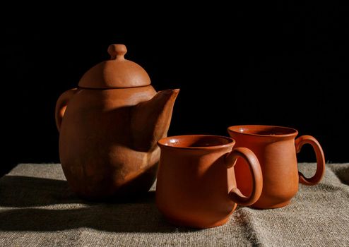 still life with a clay teapot and two cups. indoor closeup on black background